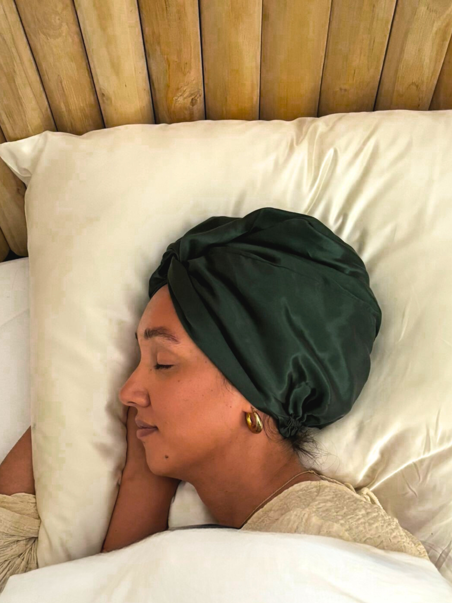 Vrouw met donkergroene zijden bonnet slapend op ivoorkleurige kussensloop – luxe zelfzorgmoment van Empowherment in Nederland
